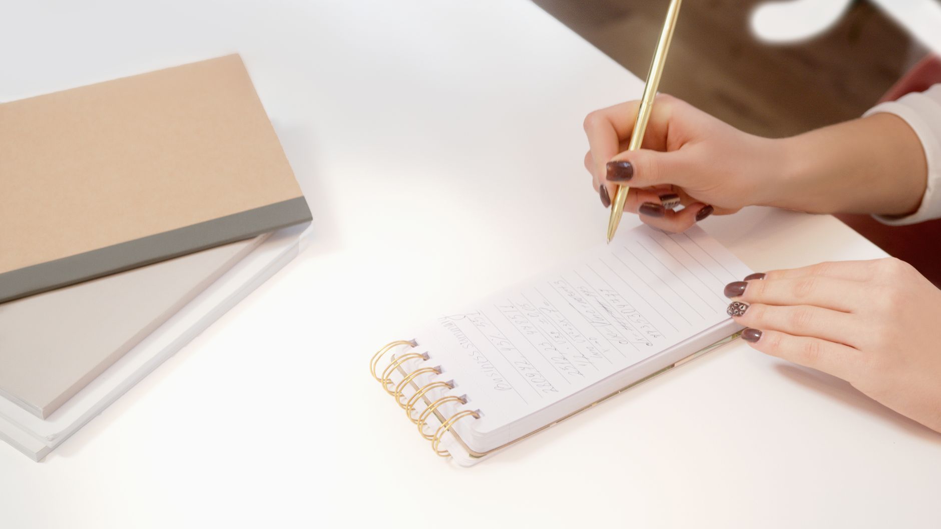 Close-up of hands writing notes in a spiral notebook while planning a client website.